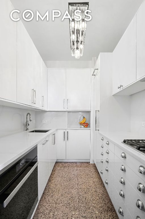 kitchen with stainless steel gas stovetop, sink, white cabinets, and black oven