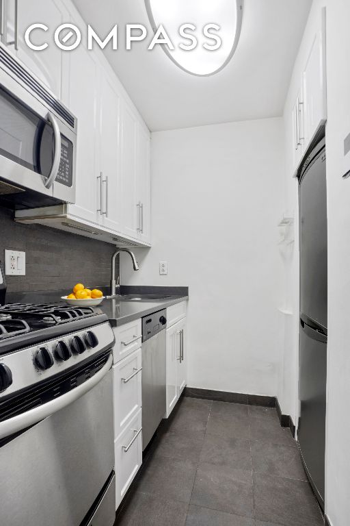 kitchen featuring white cabinetry, sink, dark tile patterned flooring, decorative backsplash, and stainless steel appliances