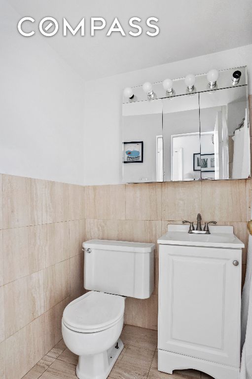 bathroom featuring tile walls, vanity, tile patterned floors, and toilet