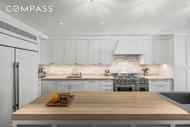 kitchen featuring a sink, white cabinetry, light countertops, high end appliances, and custom range hood