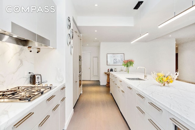 kitchen featuring sink, white cabinets, light hardwood / wood-style floors, stainless steel appliances, and light stone countertops