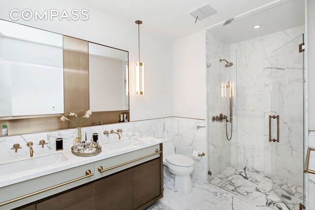 bathroom with vanity, toilet, a shower with door, and tile walls