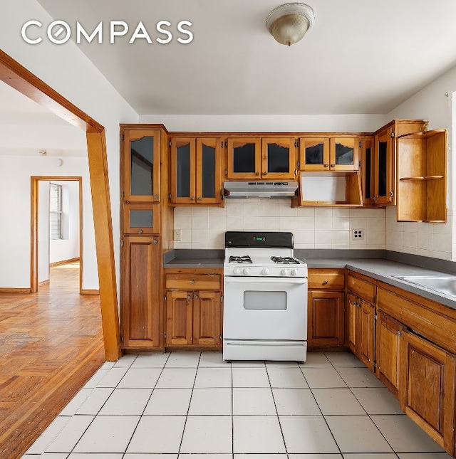 kitchen with white gas range, decorative backsplash, sink, and light tile patterned flooring