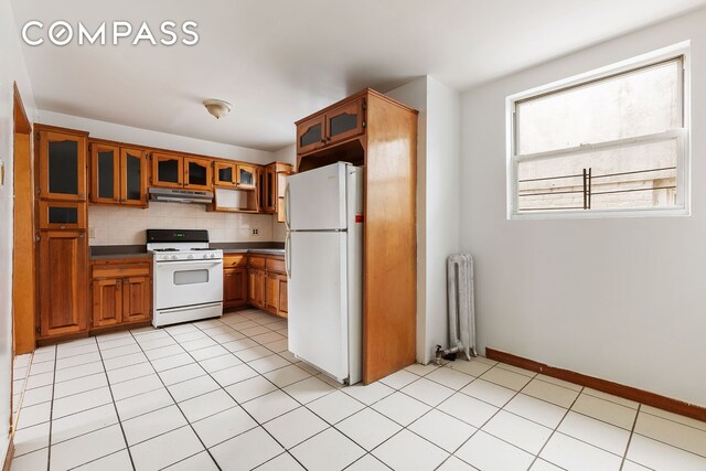 kitchen featuring white appliances, radiator heating unit, decorative backsplash, and light tile patterned floors