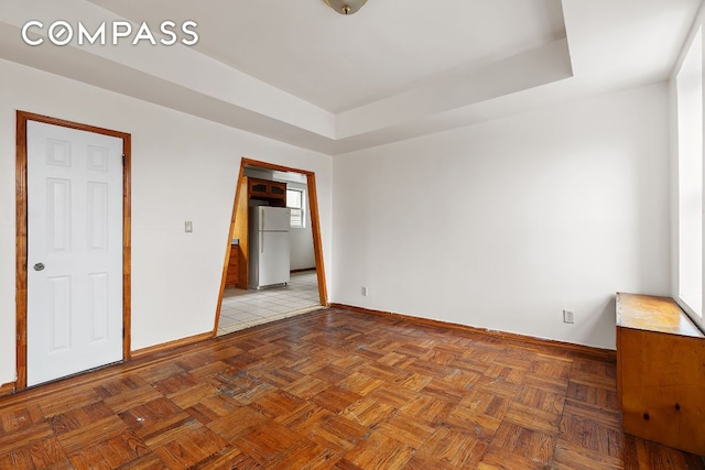 unfurnished bedroom with white refrigerator, a raised ceiling, and light parquet floors