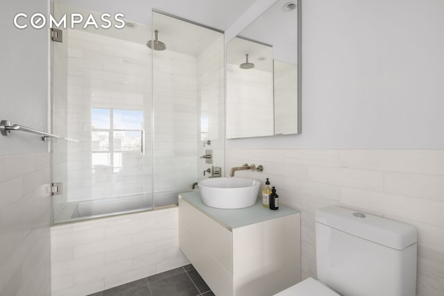 full bathroom featuring toilet, vanity, tile walls, a tile shower, and tile patterned floors