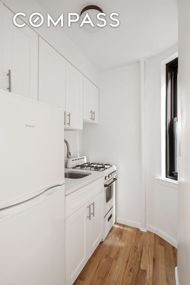 kitchen with white cabinetry, sink, white appliances, and light hardwood / wood-style flooring