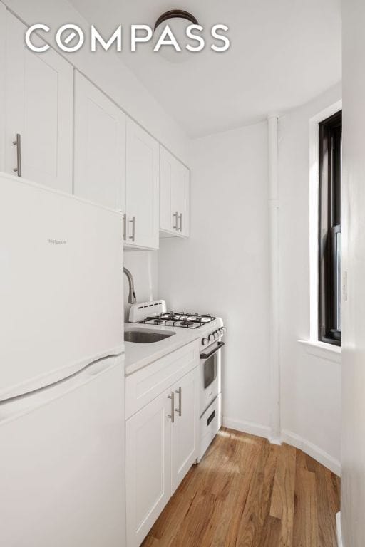 kitchen with white cabinetry, light wood-type flooring, sink, and white appliances