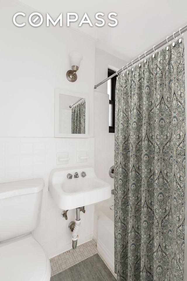 full bathroom featuring a sink, toilet, shower / bath combo with shower curtain, and tile walls