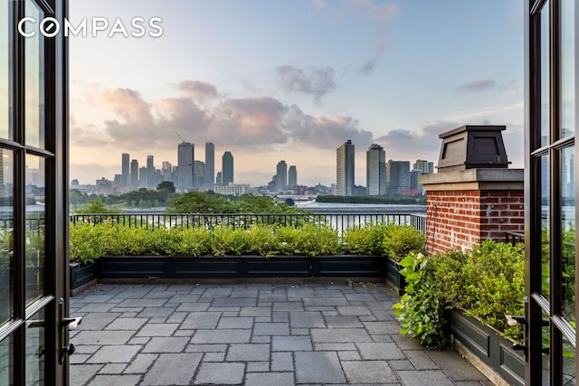 patio terrace at dusk with a water view, a view of city, and a balcony
