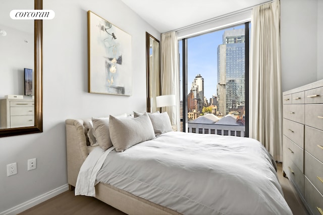 bedroom featuring a view of city, wood finished floors, and baseboards