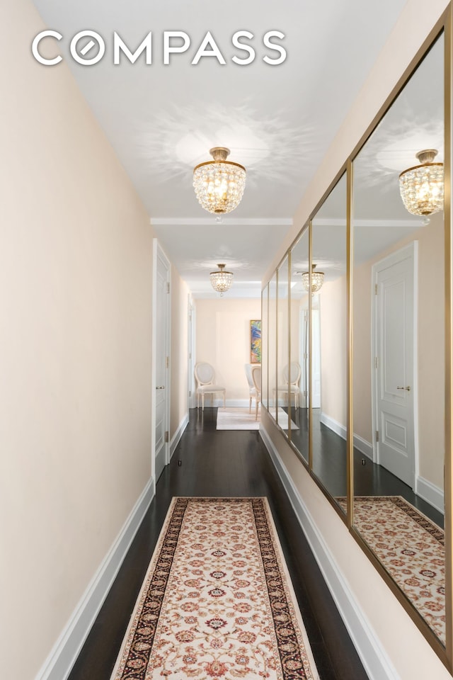 hallway with baseboards, a notable chandelier, and wood finished floors