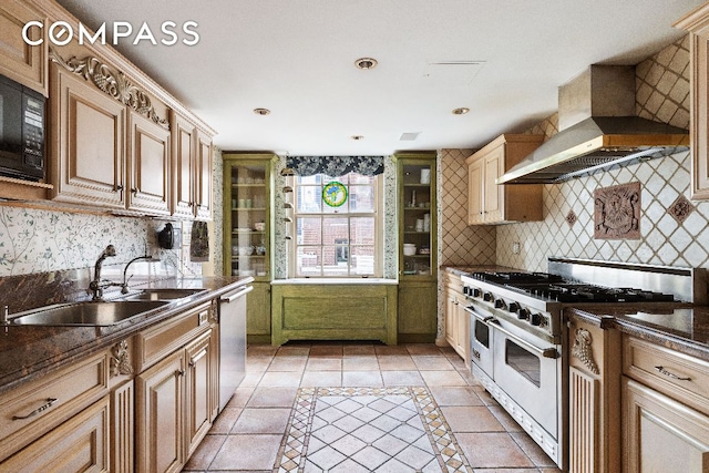 kitchen with backsplash, appliances with stainless steel finishes, light tile patterned flooring, a sink, and wall chimney exhaust hood