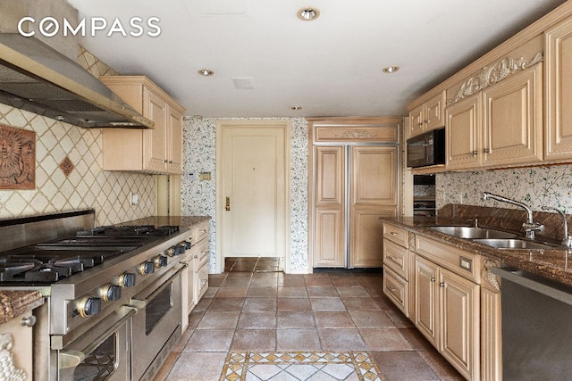 kitchen with decorative backsplash, appliances with stainless steel finishes, light brown cabinets, a sink, and wall chimney exhaust hood