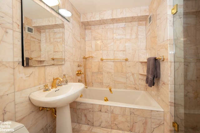 bathroom with a relaxing tiled tub, toilet, and tile walls