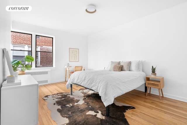 bedroom with radiator, light wood-style floors, and baseboards