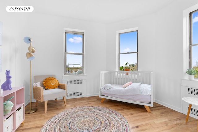 bedroom featuring radiator heating unit, wood finished floors, multiple windows, and baseboards