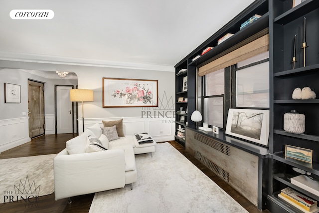 living area featuring wood finished floors, visible vents, ornamental molding, wainscoting, and a decorative wall