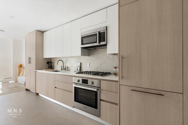 kitchen with backsplash, sink, stainless steel appliances, and white cabinetry