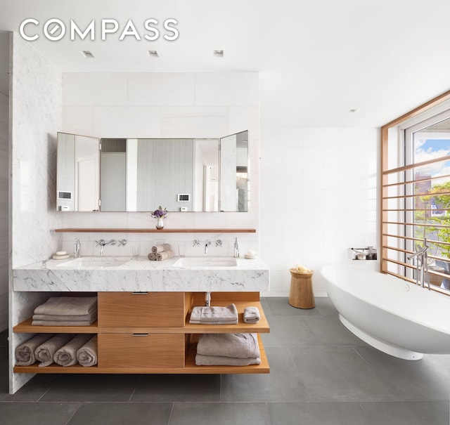 bathroom featuring double vanity, a soaking tub, a sink, and tile patterned floors