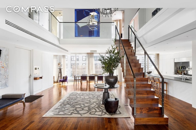 entrance foyer with a chandelier, wood finished floors, a towering ceiling, and stairs