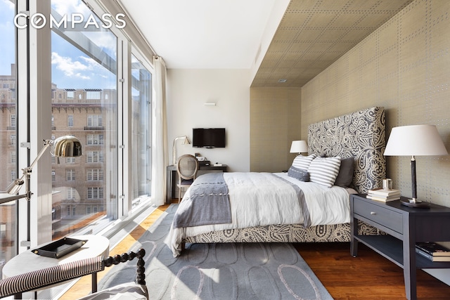 bedroom with expansive windows, access to outside, wallpapered walls, and wood finished floors