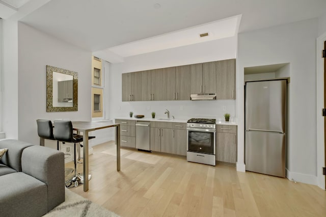 kitchen with range with gas cooktop, light countertops, freestanding refrigerator, light wood-type flooring, and under cabinet range hood