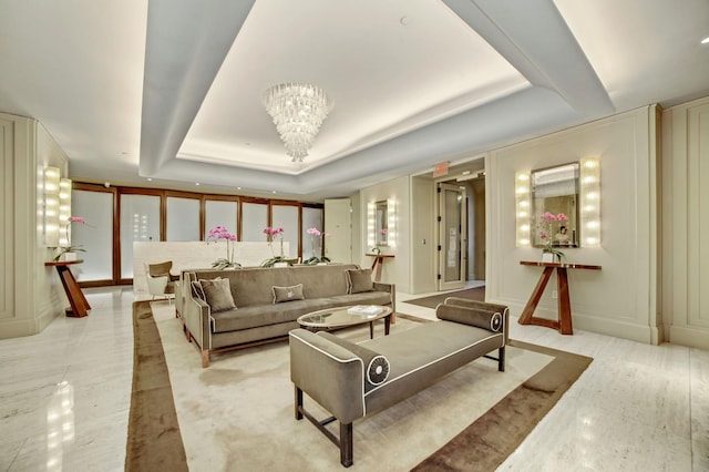 living area with a chandelier, a tray ceiling, and a decorative wall