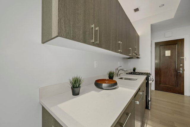 kitchen featuring dark brown cabinetry, visible vents, light wood-style floors, light countertops, and stainless steel gas range