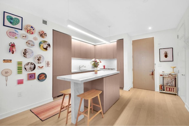 kitchen featuring light wood-type flooring, a kitchen bar, a center island, and sink