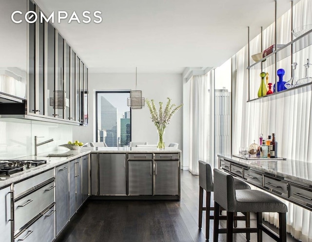 kitchen with a peninsula, gray cabinets, dark wood-style flooring, a sink, and stainless steel gas stovetop