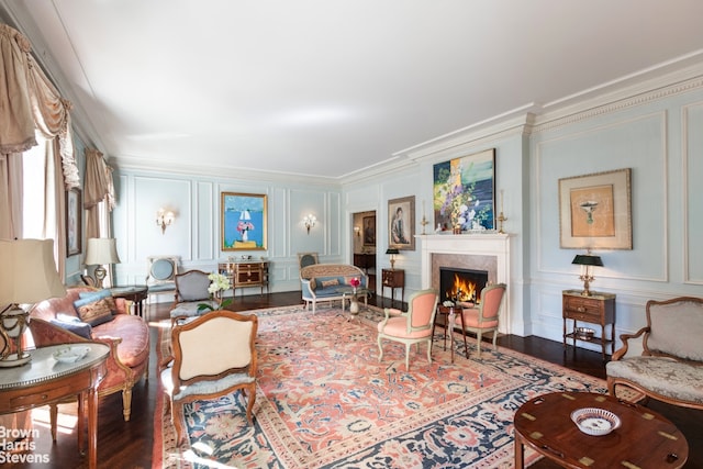 living area with ornamental molding, a fireplace, a decorative wall, and wood finished floors