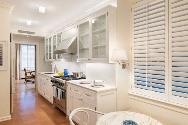 kitchen with sink, stainless steel range, ornamental molding, wall chimney range hood, and white cabinets