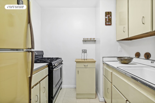 kitchen with a sink, freestanding refrigerator, gas stove, light tile patterned flooring, and light countertops