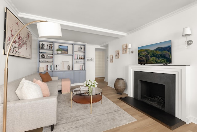 living room with light wood-style floors, a fireplace with raised hearth, ornamental molding, and baseboards