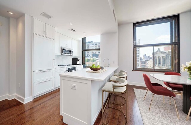 kitchen featuring a breakfast bar area, a kitchen island with sink, white cabinetry, backsplash, and dark hardwood / wood-style flooring