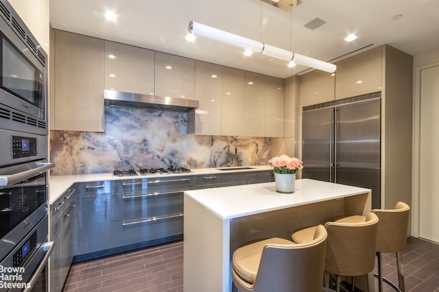 kitchen featuring backsplash, extractor fan, a center island, built in appliances, and a kitchen breakfast bar