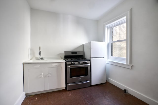 kitchen with stainless steel gas stove, baseboards, a sink, and freestanding refrigerator