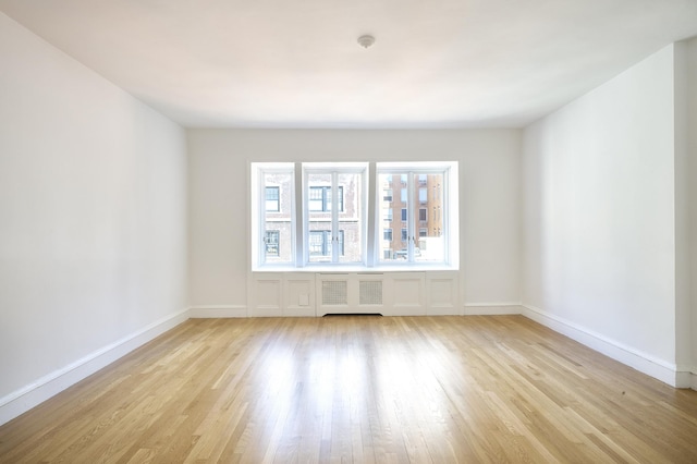 empty room featuring baseboards, light wood finished floors, and radiator