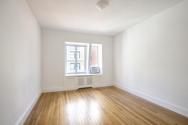 spare room with light wood finished floors, radiator heating unit, baseboards, and cooling unit