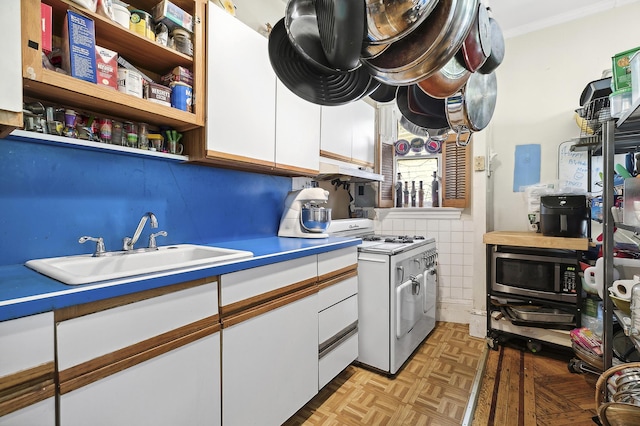 kitchen featuring ornamental molding, white gas range, white cabinets, tile walls, and a sink