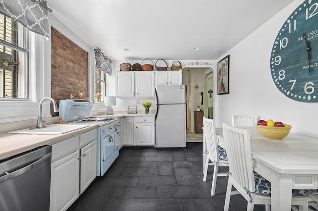 kitchen with a sink, stone tile floors, white cabinetry, appliances with stainless steel finishes, and light countertops