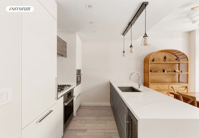 kitchen with white cabinets, appliances with stainless steel finishes, sink, hanging light fixtures, and light hardwood / wood-style flooring