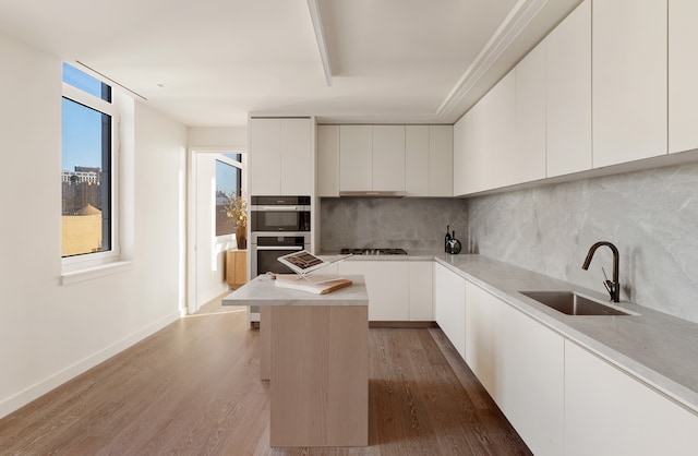 kitchen with gas stovetop, modern cabinets, stainless steel double oven, a sink, and wood finished floors