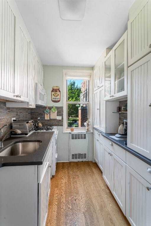 5650 Netherland Ave Unit 1A, New York City, NY 10471 - kitchen with radiator, dark countertops, white microwave, a sink, and backsplash