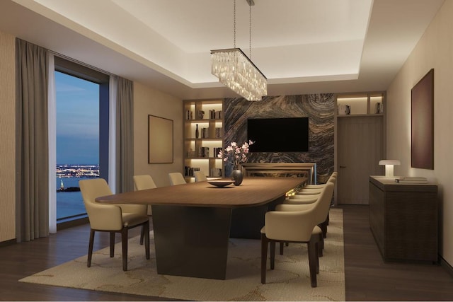 dining area with an accent wall, a tray ceiling, dark wood-type flooring, and a water view