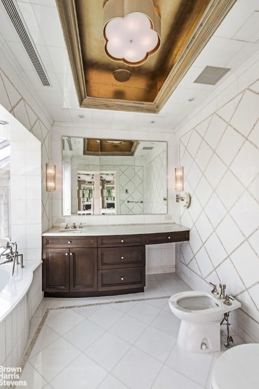 bathroom featuring a raised ceiling, ornamental molding, a bidet, and tile walls