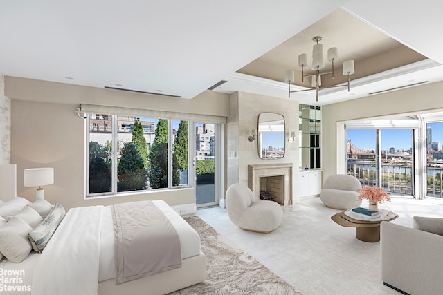 bedroom featuring a premium fireplace, access to exterior, a water view, a tray ceiling, and light colored carpet