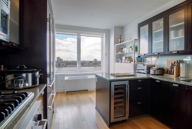 kitchen with light stone counters, wine cooler, light wood finished floors, radiator, and appliances with stainless steel finishes