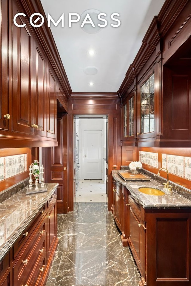 kitchen with glass insert cabinets, ornamental molding, stone counters, marble finish floor, and a sink